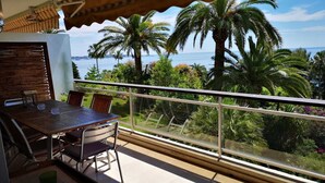 A balcony with a table and chairs, overlooking a coastal landscape with palm trees and a view of the sea. - Luxury building with swimming pool and sea access (Vallauris)