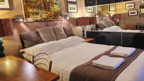 A hotel room with a large bed, a wooden nightstand, a mirror, and artwork on the walls. - Lovely 3 bedroom bungalow in Keswick with gardens and ample off road parking (Keswick)
