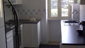 A compact kitchen with white cabinets, a stove, and a window with a view of trees. - ROMAN HOLIDAYS, TWO STEPS FROM SAN PIETRO FULL OPTIONALS (Roma)