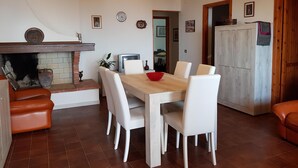 A dining area with a wooden table, white chairs, a red bowl, a television, and a fireplace with a brick surround.