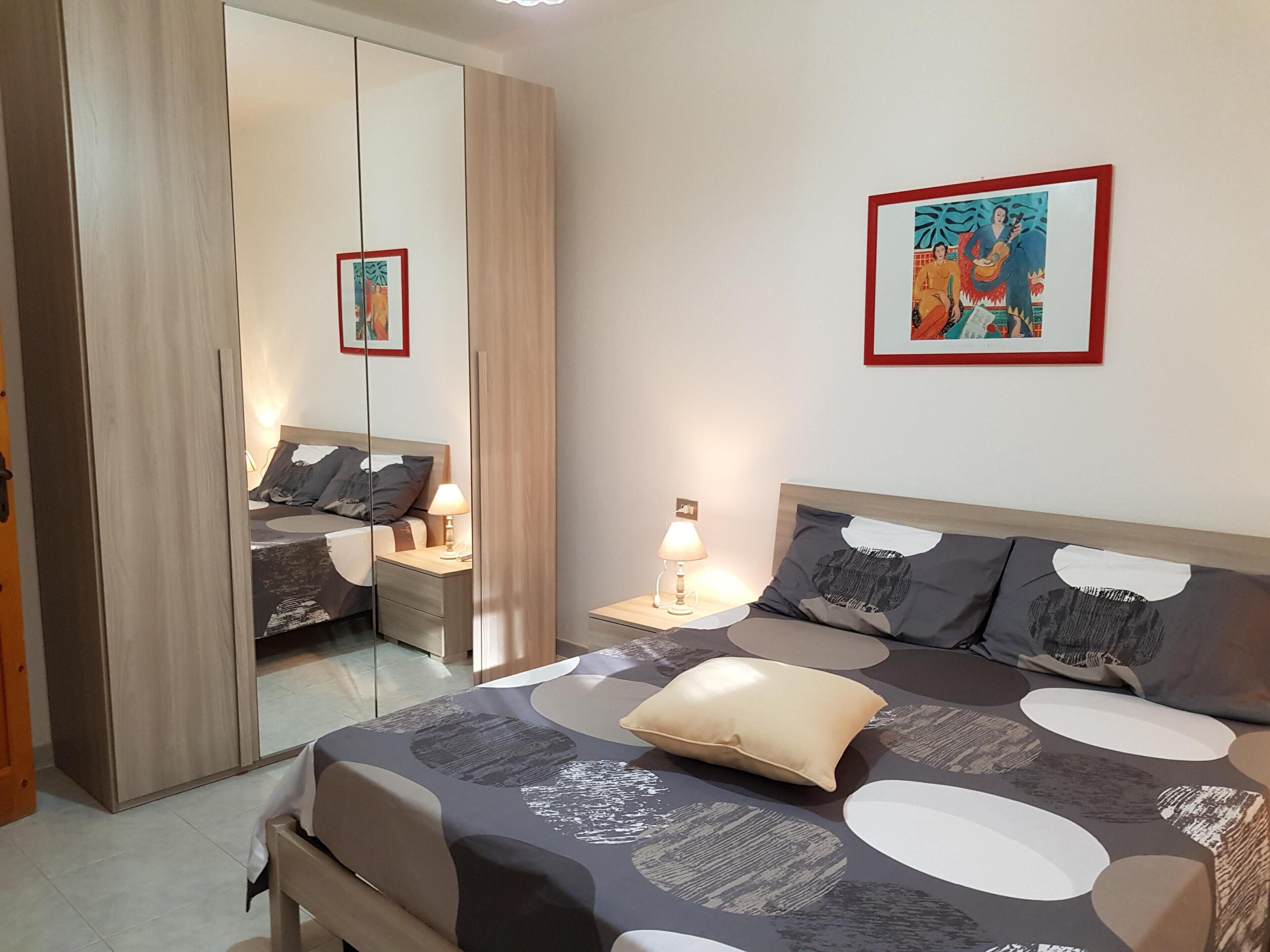 A modern bedroom with a large bed, bedside tables with lamps, a wardrobe, and a framed picture on the wall.