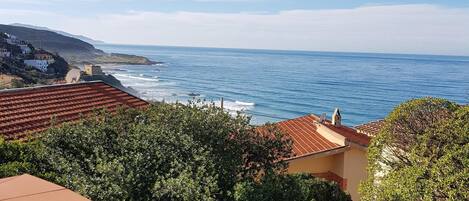 Vista costera con una parrilla para barbacoa, cielo despejado y una línea de costa distante.
