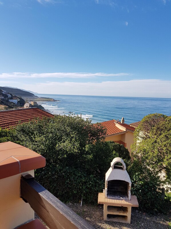 A coastal view with a barbecue grill, a clear sky, and a distant shoreline.
