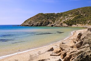 A beach with clear water, rocky terrain, and a hilly backdrop. - Marina Di Arbus: apartment/ flat - Arbus (ARBUS)