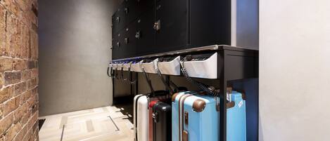 A row of suitcases on a rack in a hallway with a brick wall and a wooden floor.