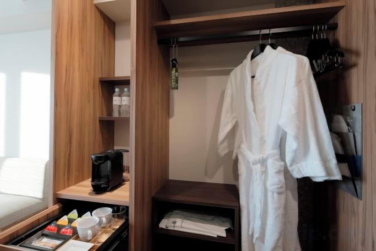 Un placard en bois dans lequel est suspendue une robe, une machine à café et un plateau avec des tasses et une bouilloire.