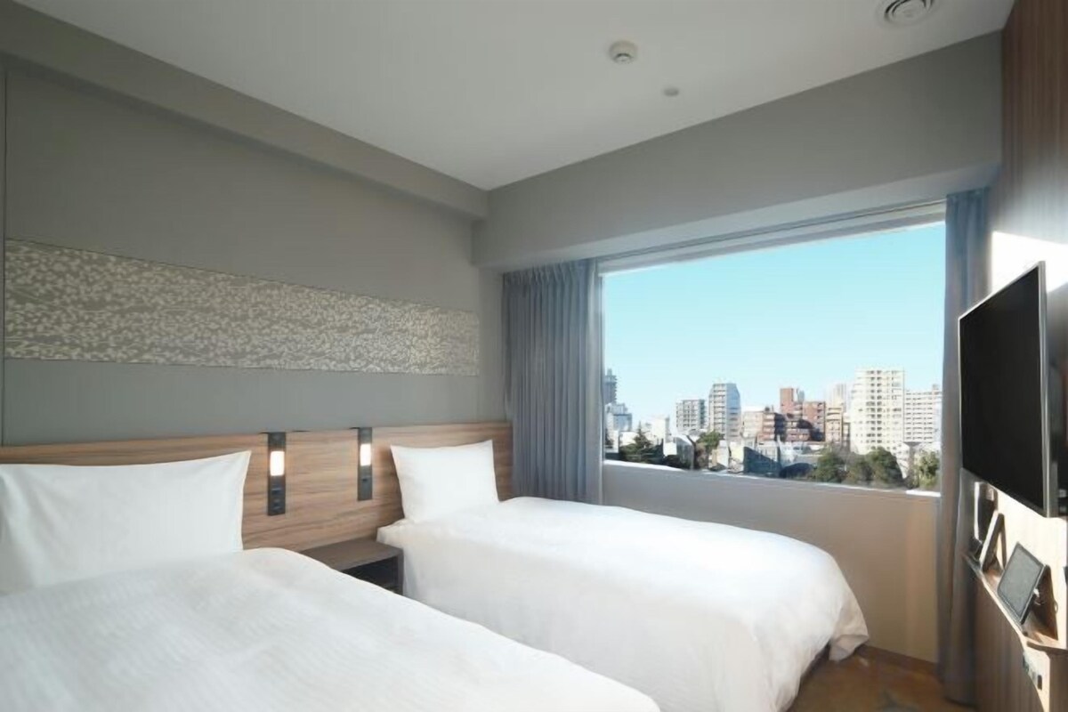 Une chambre d’hôtel avec deux lits, une grande fenêtre donnant sur la ville et un téléviseur à écran plat.