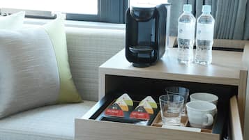 A hotel room with a coffee maker, water bottles, and a drawer containing tea bags and glasses.