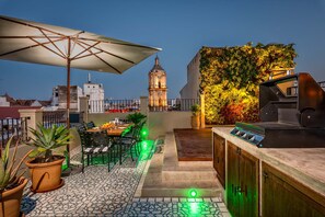 Un patio al aire libre con una mesa de comedor, sillas, una sombrilla y una parrilla.