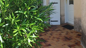 A courtyard with a tiled floor, a potted plant, and a building with a white door and window. - Sainte Maxime: House with garden on french riviera. Terrace with solarium (Sainte-Maxime)
