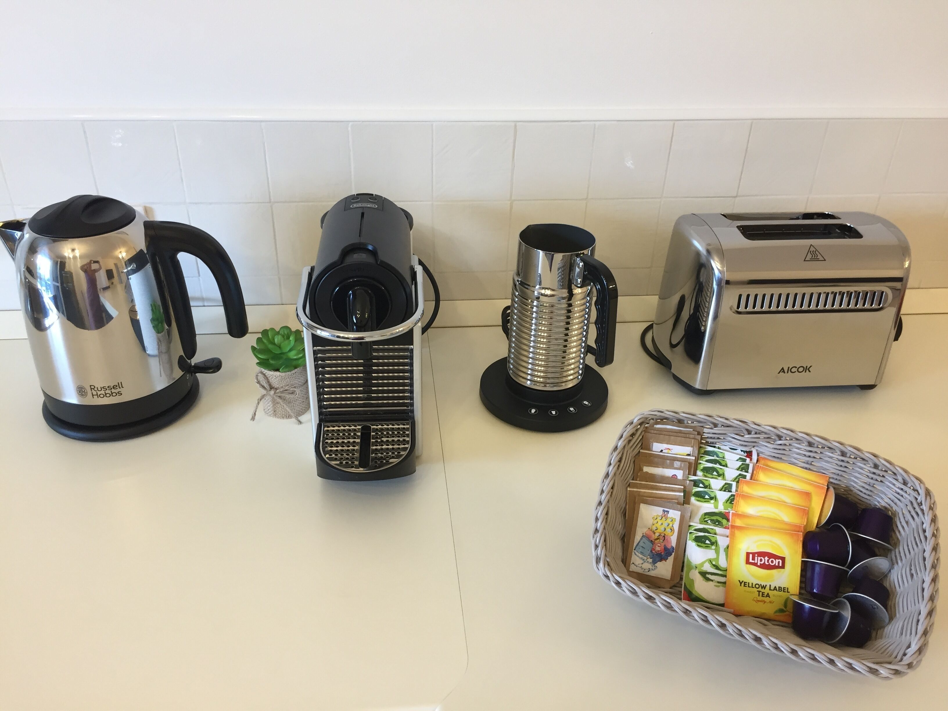 En køkkenbordplade med elkedel, kaffemaskine, brødrister og en kurv med Lipton teposer.