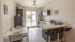 Une cuisine moderne avec un coin repas, comprenant un îlot central doté de tabourets, une cuisinière à gaz et une fenêtre laissant entrer la lumière naturelle.