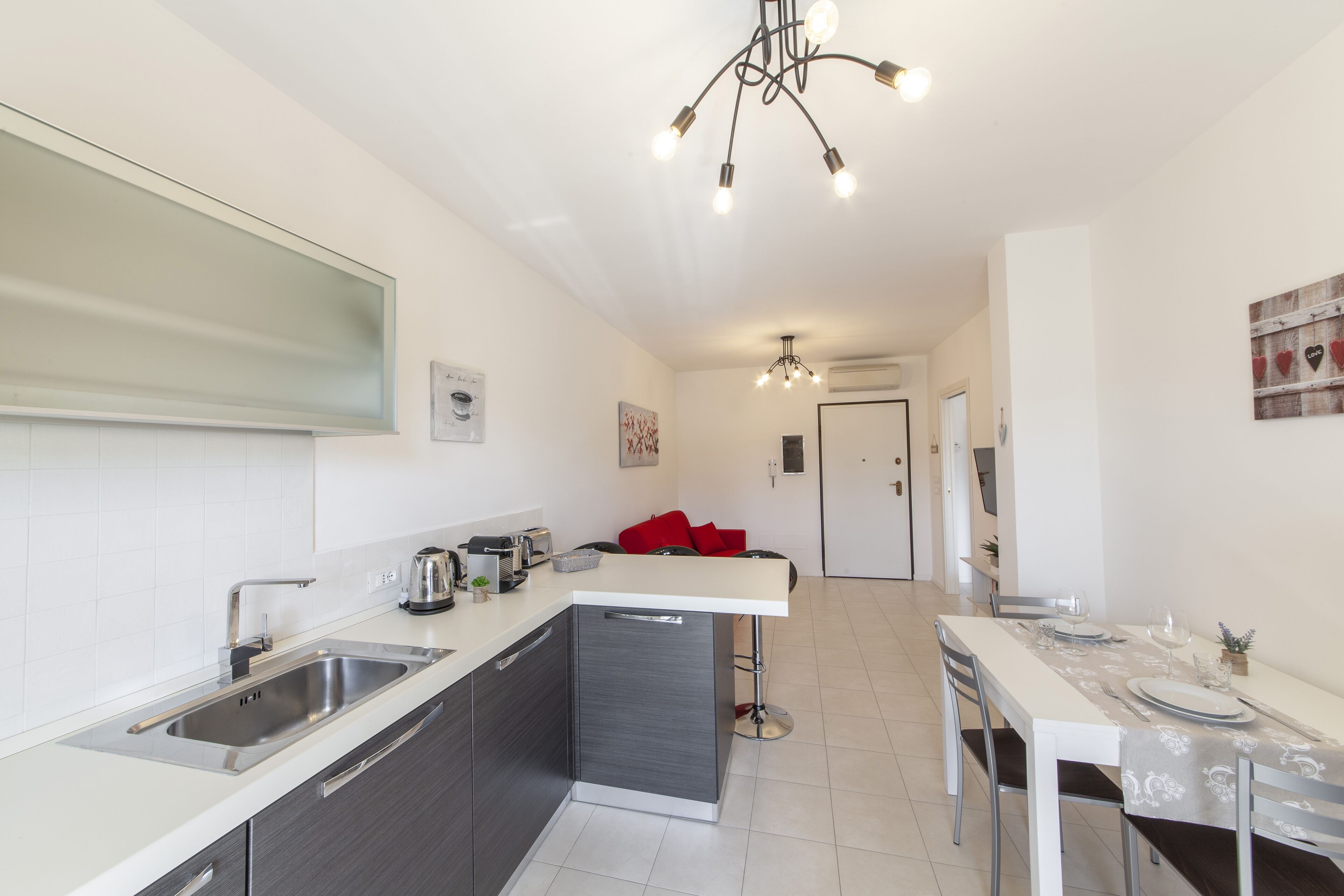 Una cocina moderna con una isla central, un comedor con mesa para dos personas y un pasillo que conduce a un dormitorio.