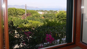 A balcony with a view of a coastal landscape, including greenery and a distant sea.