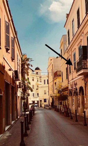 A narrow street lined with buildings, some with balconies and others with shutters.