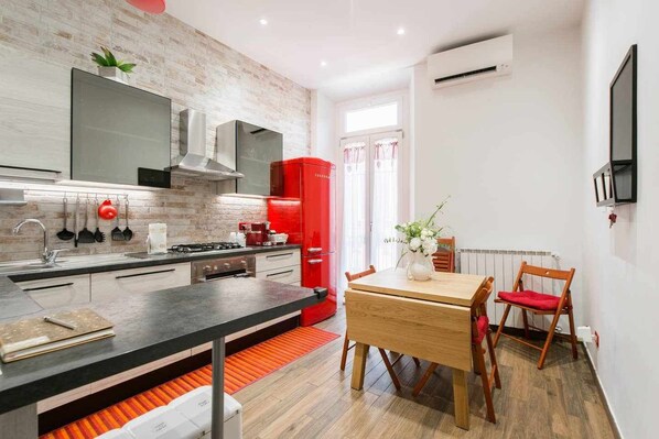 A modern kitchen with a red refrigerator, a dining table with chairs, and a small dining area with a window.