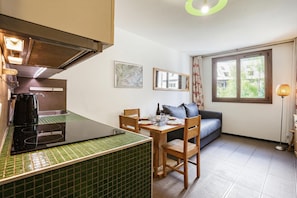 Une cuisine de taille réduite comprenant une cuisinière, une table à manger avec des chaises, un canapé et une fenêtre avec des rideaux.