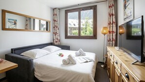 A hotel room with a bed, a desk, a TV, and a window with curtains. - Cham Sud F210 Mountain View for 4, Chamonix, France (Chamonix)