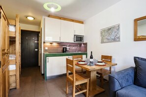 A compact kitchen with a microwave, wooden cabinets, and a dining table with chairs.