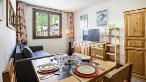 A dining area with a table set for four, a sofa, a television, and a wooden cabinet. - Cham Sud F210 Mountain View for 4, Chamonix, France (Chamonix)