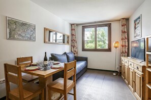 En spiseplads med et bord dækket til to personer, en sofa, et fjernsyn og et skab.