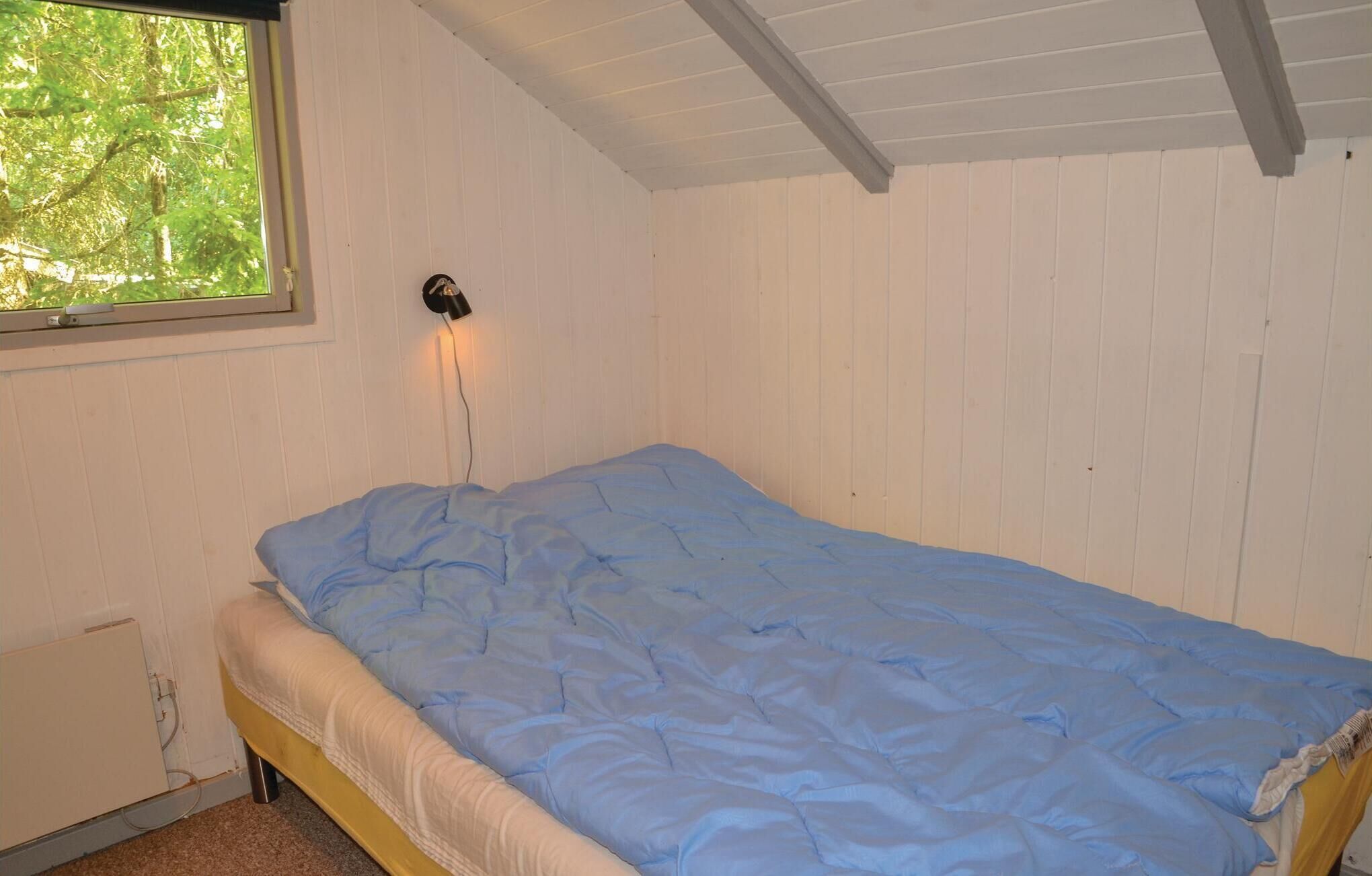 Un llit individual amb matalàs blau en una habitació amb parets de taules blanques i sostre inclinat.