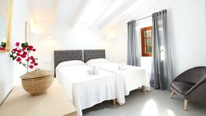 A hotel room with two beds, a large mirror, a wicker basket with flowers, a chair, and a window with curtains. - Finca Ramona, Pool, 6 bedrooms , A / C, Wi-Fi, smart TV (Pollença)