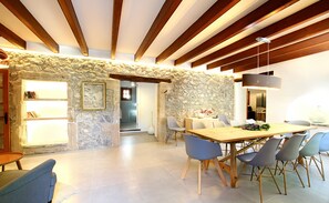 A dining area with a stone wall, wooden beams, and a modern chandelier.