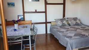A bedroom with a bed, a small table with chairs, a vase with flowers, and a picture on the wall.