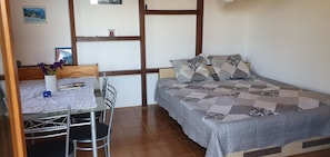A bedroom with a bed, a small table with chairs, a vase with flowers, and a picture on the wall.
