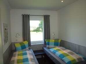 A room with two beds, each with a checkered bedspread and pillows, a window with curtains, a wall-mounted lamp, and a bicycle art piece.