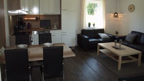 A modern kitchen with white cabinets, a dining table with chairs, a black sofa, and a coffee table.