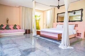 A bedroom with a bed, a bench with cushions, a large mirror, and a view of greenery outside.