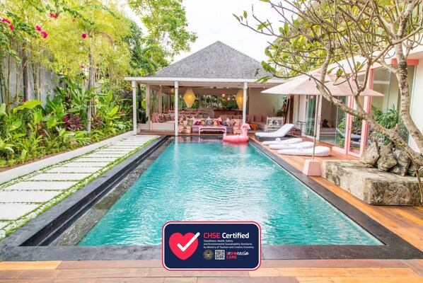 A CHSE certified pool area with a covered seating area, lounge chairs, and a view of the surrounding garden.