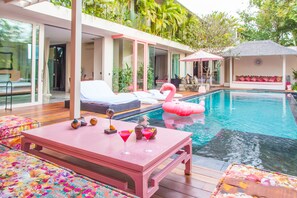 A poolside area with a pink table, lounge chairs, and a flamingo float.