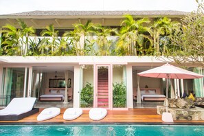 A hotel with a pool, two bedrooms, a staircase, and a balcony with plants.