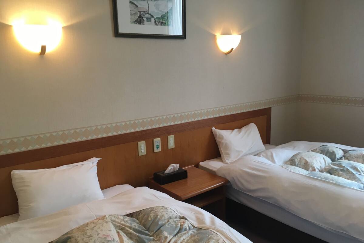 Une chambre d’hôtel avec deux lits, une table de chevet et des lampes fixées au mur.