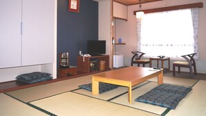 A traditional Japanese-style living room with tatami flooring, a low wooden table, a television, and a view of the outside through a large window. - Breezbay Resort Kurohime (Shinano)
