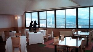 A dining area with tables and chairs, large windows, and a view of the cityscape. - Breezbay Resort Kurohime (Shinano)
