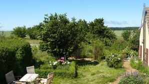 Ein Garten mit Tisch und Stühlen, umgeben von üppigem Grün und Blumen.