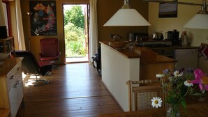 Eine geräumige Küche mit Holzboden, ein Essbereich mit Holztisch und Blick ins Freie durch eine Glastür.