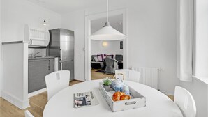 A modern kitchen with a refrigerator, stove, and white cabinetry. There is a dining area with a white table, chairs, and a tray with bread and flowers. - 1 bedroom cozy apartment in Svendborg (Svendborg)