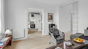 A modern living room with a wicker chair, a sofa, a dining table with fruit and glasses, and a kitchen in the background. - 1 bedroom cozy apartment in Svendborg (Svendborg)