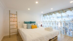 A bedroom with a wooden bed, white bedding, teal and yellow pillows, a ladder, and a window with a decorative curtain. - Shanghai Moxi Inn Huaihai Rd No.3 Branch (Shanghai)