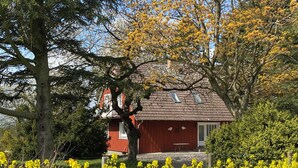 Een rode woning met pannendak, omgeven door gele bloemen en bomen.