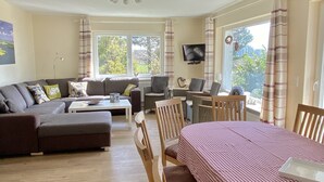 Een ruime woonkamer met een zithoek, een eettafel met stoelen en een plafondventilator.