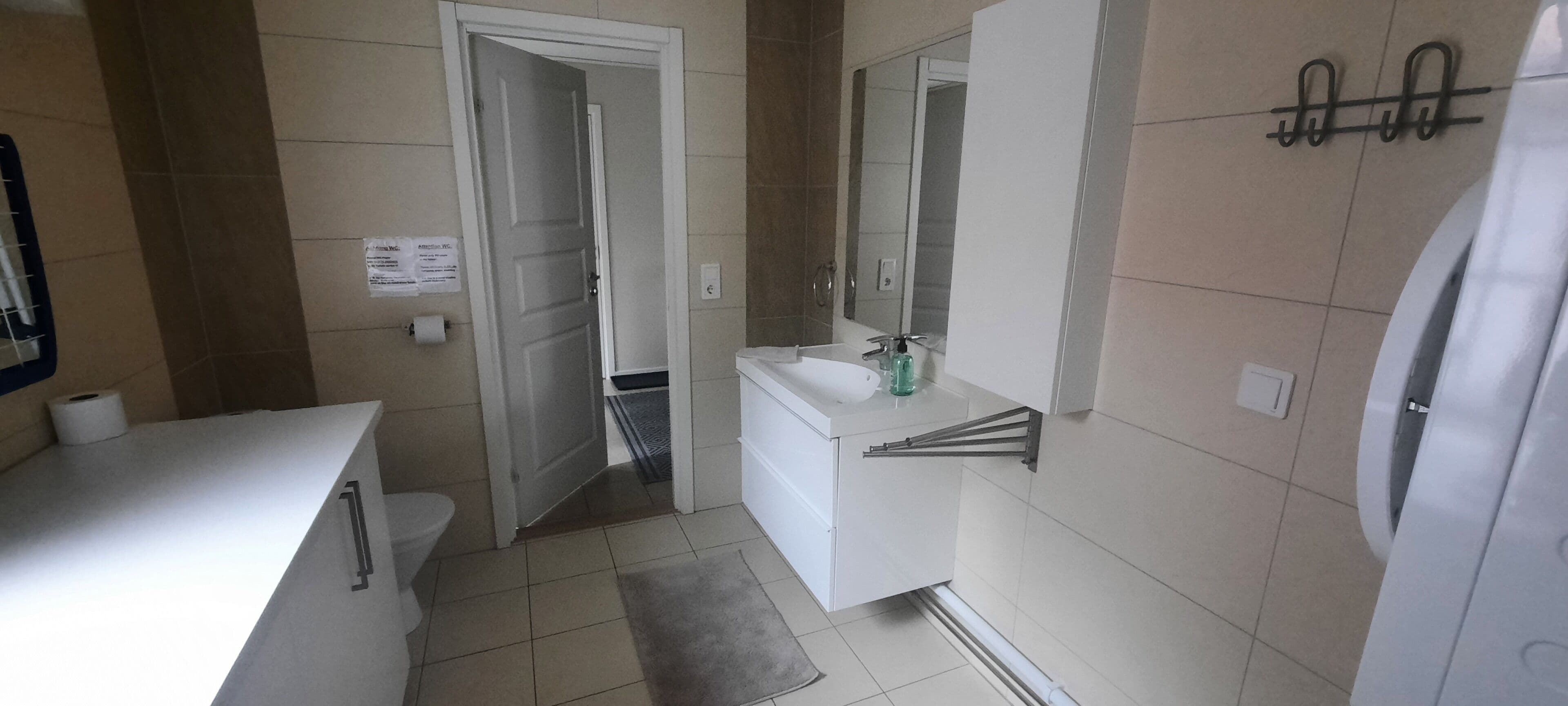 A modern bathroom with a toilet, sink, and mirror. There is a towel rack on the wall and a door leading to another room.