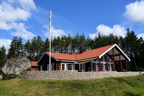 Eine Hütte mit steinernen Fundamenten und einem roten Ziegeldach, versehen mit großen Fenstern.