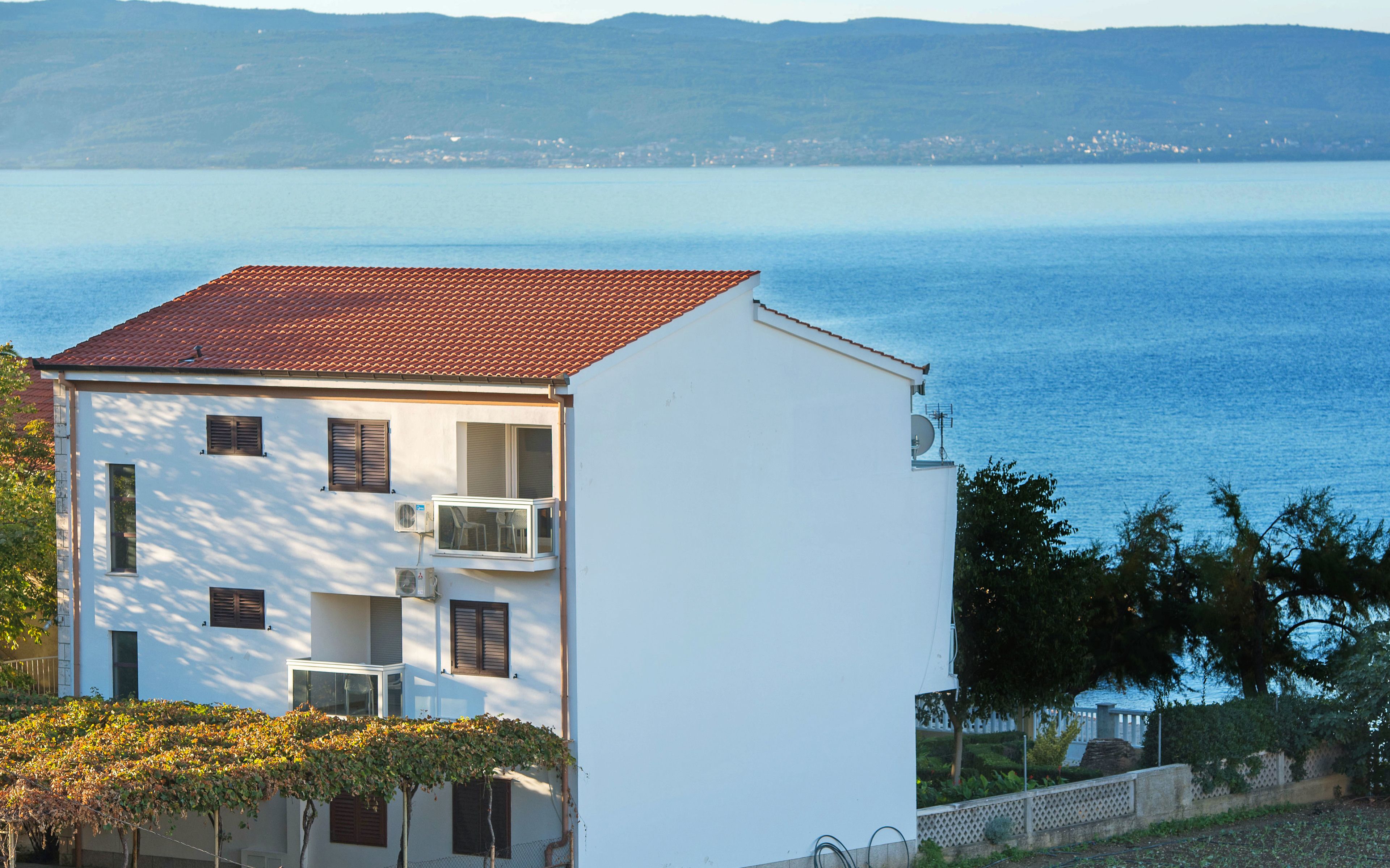 A white building with a red-tiled roof, air conditioning units, and a bay window.