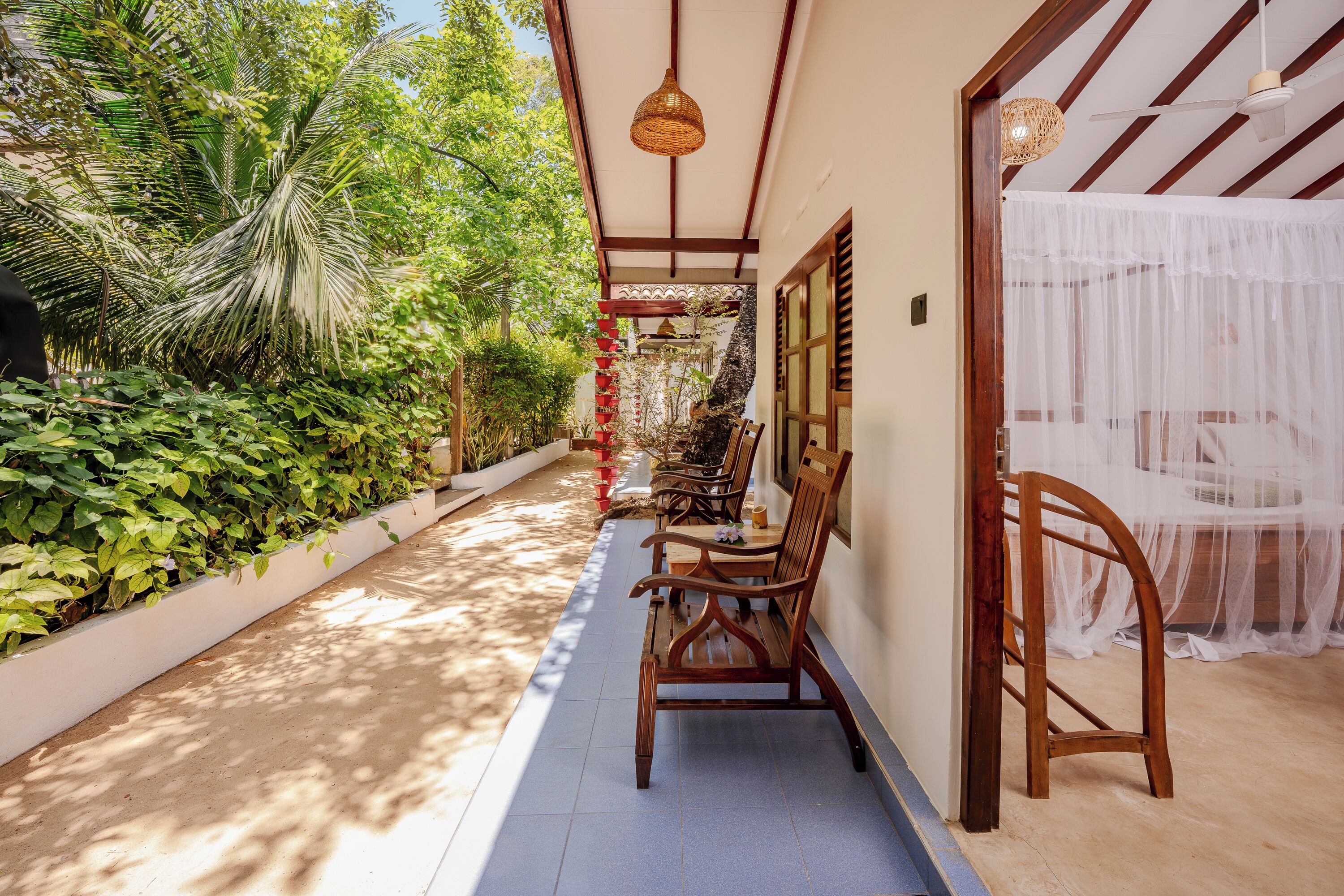 A covered outdoor seating area with wooden benches, a ceiling fan, and a view of lush greenery.